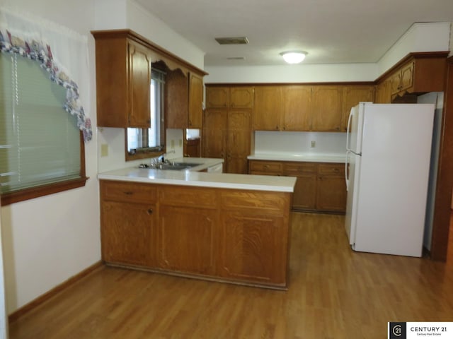 kitchen with light wood finished floors, light countertops, brown cabinets, a peninsula, and freestanding refrigerator