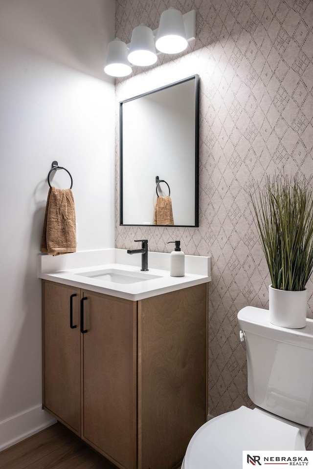 half bathroom featuring baseboards, toilet, wood finished floors, and vanity