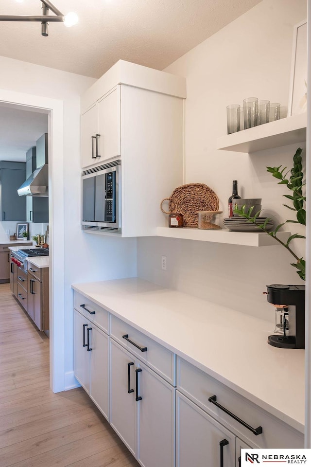 kitchen with light wood finished floors, wall chimney range hood, light countertops, appliances with stainless steel finishes, and white cabinets