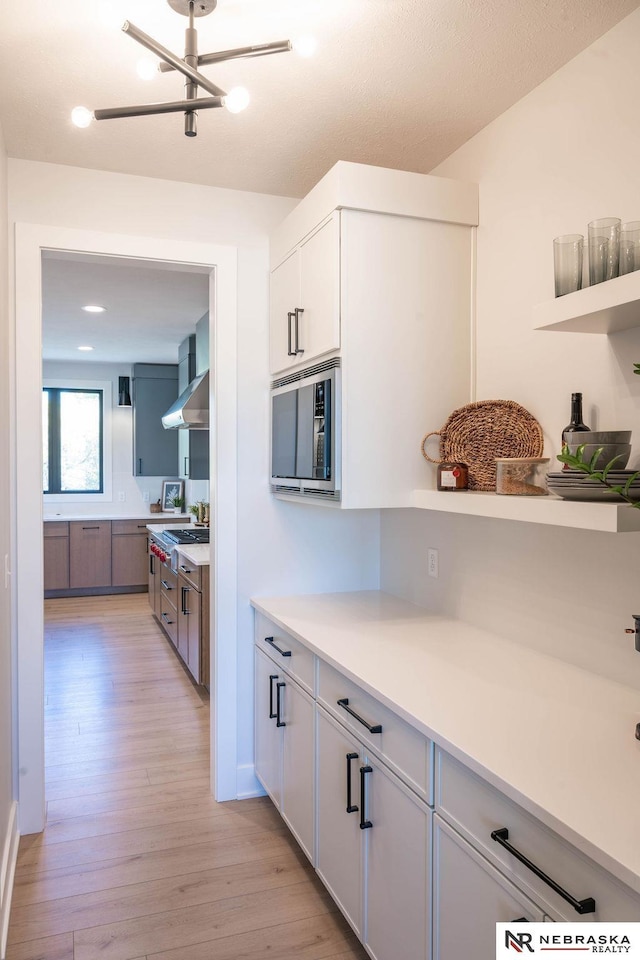 kitchen featuring light wood finished floors, a chandelier, light countertops, appliances with stainless steel finishes, and white cabinetry