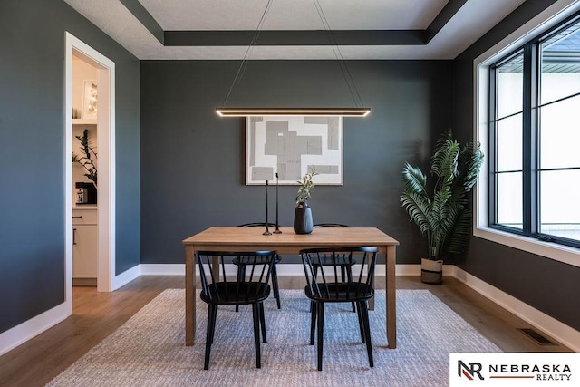 dining area with a tray ceiling, baseboards, visible vents, and wood finished floors