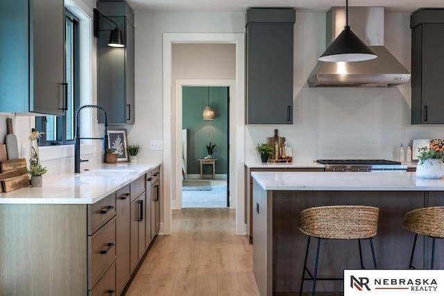 kitchen featuring light stone countertops, a breakfast bar, a sink, wall chimney range hood, and backsplash