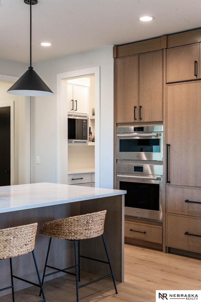 kitchen with a breakfast bar, light wood-style flooring, recessed lighting, double oven, and built in microwave