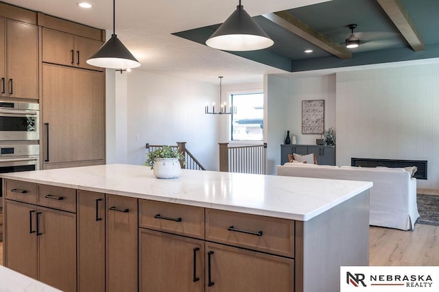 kitchen featuring decorative light fixtures, beamed ceiling, light wood-type flooring, light stone counters, and stainless steel double oven