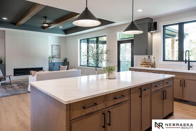 kitchen with a kitchen island, light wood-style flooring, a sink, open floor plan, and a large fireplace