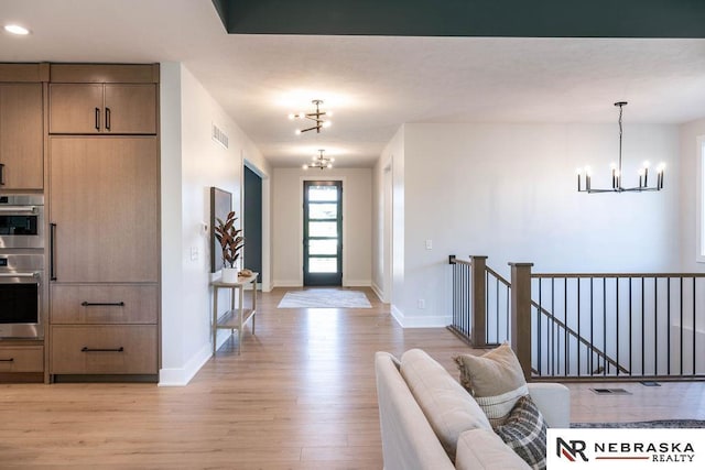 foyer entrance featuring light wood-type flooring, baseboards, an inviting chandelier, and visible vents