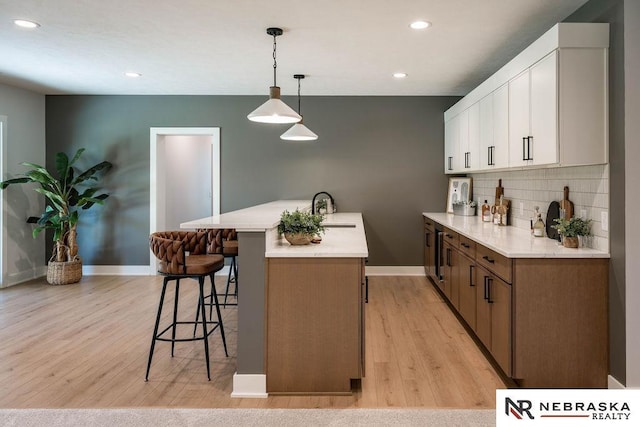 kitchen featuring a breakfast bar, light wood-style floors, backsplash, and a sink