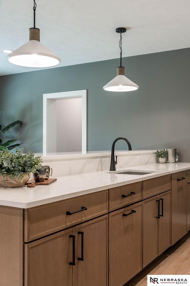 kitchen with decorative light fixtures, light stone counters, light wood-style floors, and a sink