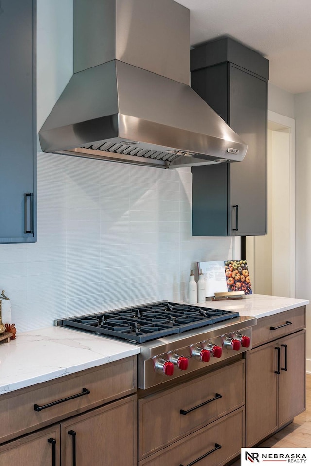 kitchen with stainless steel gas cooktop, light stone countertops, tasteful backsplash, and wall chimney range hood