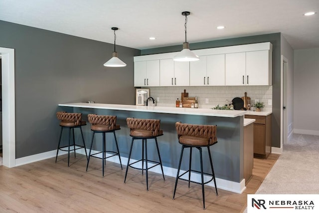 kitchen with white cabinetry, light wood finished floors, decorative backsplash, hanging light fixtures, and a kitchen bar