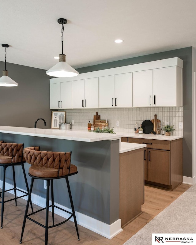 kitchen featuring light wood-type flooring, a breakfast bar, light countertops, decorative light fixtures, and tasteful backsplash