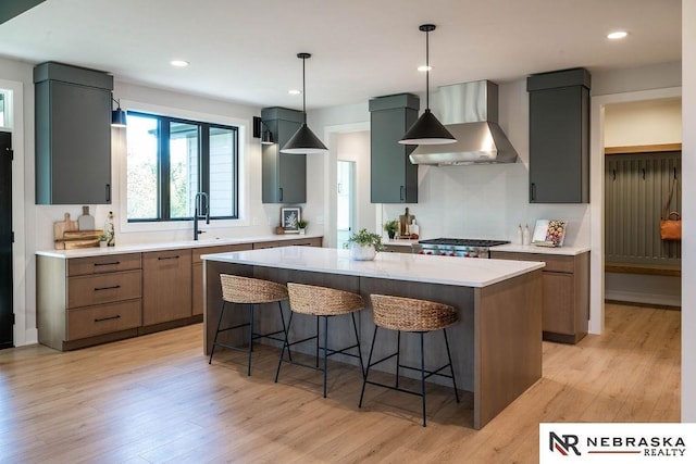 kitchen with light wood finished floors, a breakfast bar, wall chimney exhaust hood, and light countertops