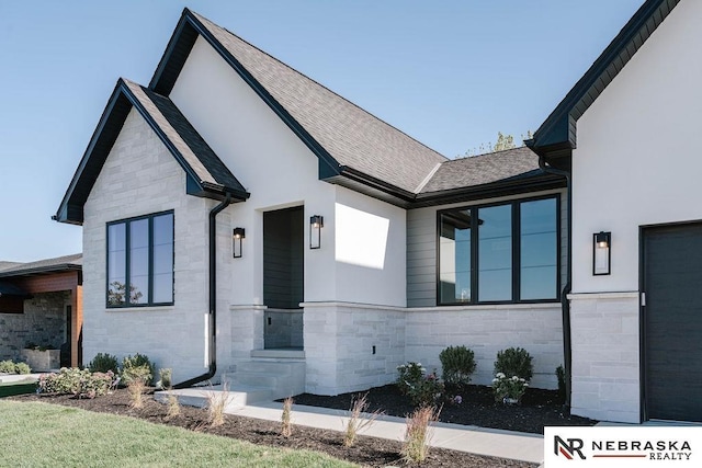 contemporary house with stone siding, stucco siding, and roof with shingles