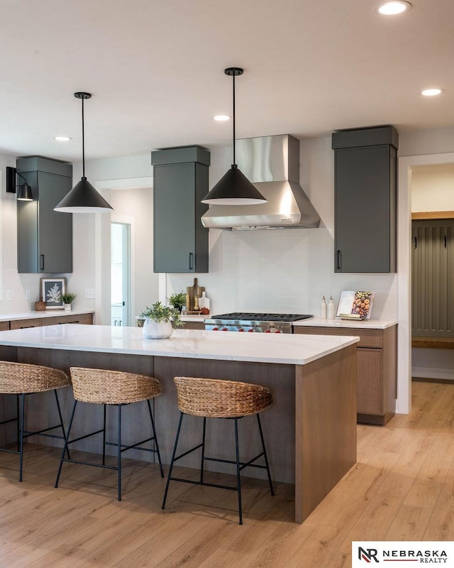 kitchen with tasteful backsplash, stainless steel gas cooktop, light wood-type flooring, a kitchen breakfast bar, and wall chimney exhaust hood