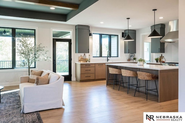 kitchen with a kitchen breakfast bar, light wood-style flooring, light countertops, and wall chimney range hood