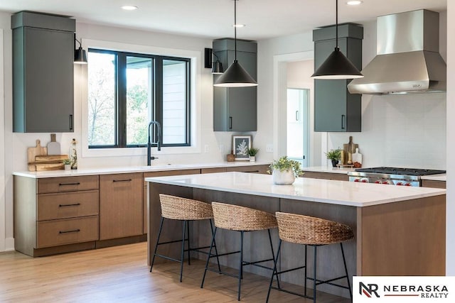 kitchen featuring tasteful backsplash, a breakfast bar area, wall chimney exhaust hood, and light wood-type flooring