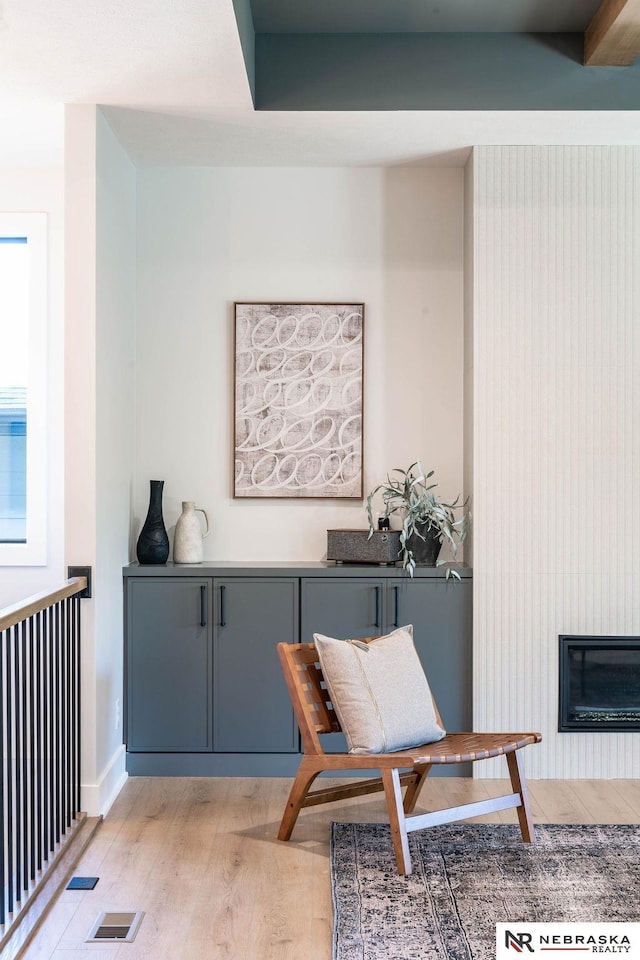 sitting room with light wood finished floors, visible vents, baseboards, and a glass covered fireplace