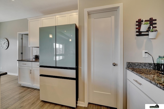 kitchen featuring baseboards, light wood-style flooring, dark stone countertops, freestanding refrigerator, and white cabinetry