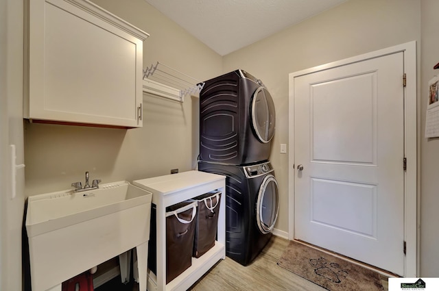 laundry area with a sink, cabinet space, light wood-style floors, and stacked washer and clothes dryer