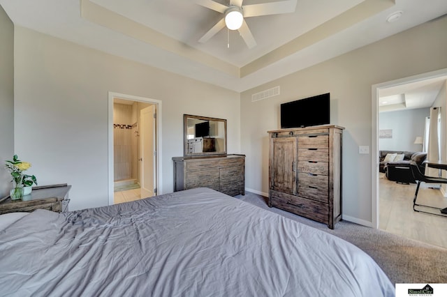 carpeted bedroom with visible vents, baseboards, ensuite bathroom, a raised ceiling, and a ceiling fan