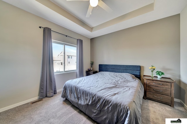 carpeted bedroom featuring visible vents, baseboards, a tray ceiling, and a ceiling fan