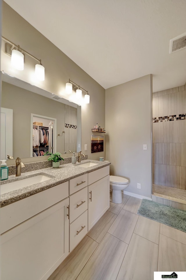 full bath with toilet, visible vents, a tile shower, and a sink