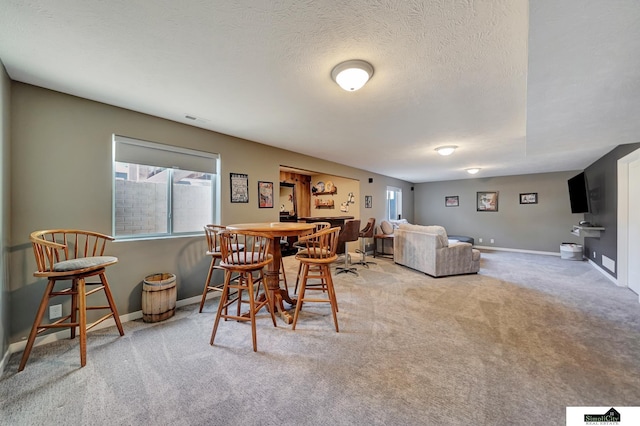 carpeted dining room featuring visible vents, bar area, a textured ceiling, and baseboards