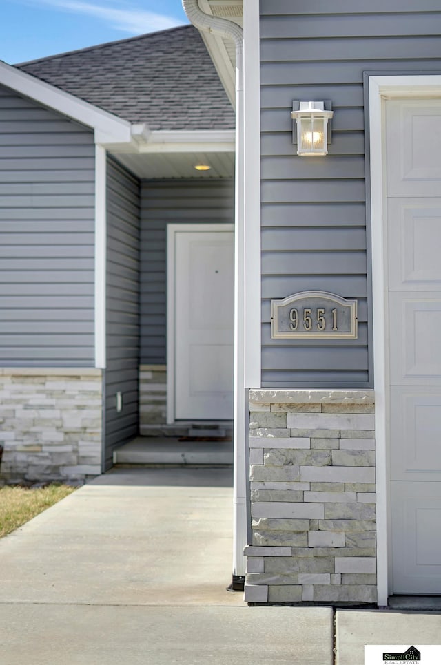 doorway to property with stone siding and a shingled roof