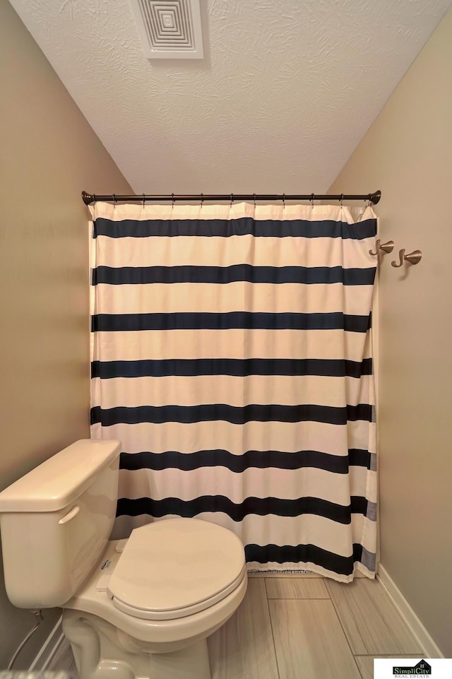 full bath featuring a shower with curtain, toilet, and a textured ceiling