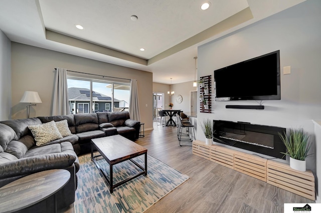 living room featuring baseboards, a tray ceiling, recessed lighting, an inviting chandelier, and wood finished floors