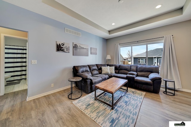 living room featuring visible vents, light wood-style flooring, a raised ceiling, and baseboards