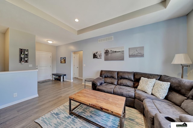 living room with a tray ceiling, visible vents, baseboards, and light wood-style flooring