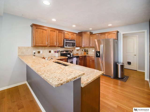 kitchen with decorative backsplash, a peninsula, light wood-style floors, stainless steel appliances, and a sink