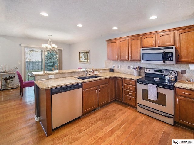 kitchen featuring light wood-type flooring, a notable chandelier, a sink, stainless steel appliances, and a peninsula