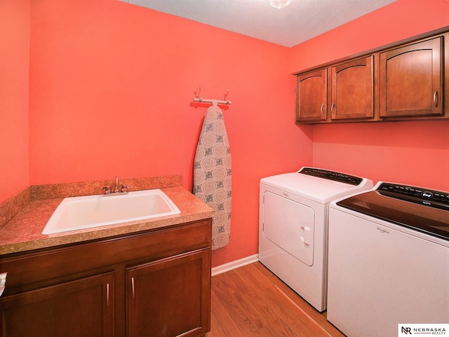 laundry room featuring a sink, cabinet space, washing machine and dryer, and light wood finished floors