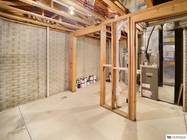 unfinished below grade area with heating unit, water heater, and brick wall