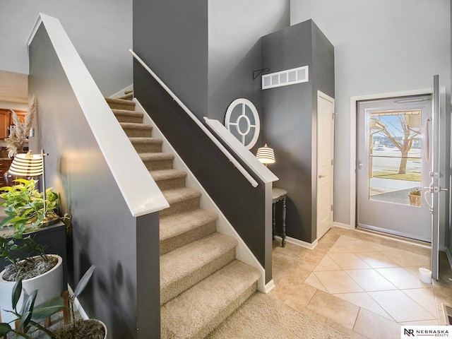 entryway with baseboards, visible vents, stairs, a towering ceiling, and tile patterned floors