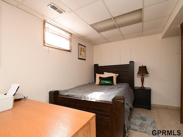 bedroom featuring light tile patterned floors, visible vents, a paneled ceiling, and baseboards