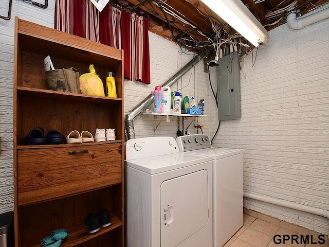 clothes washing area with light tile patterned floors, brick wall, laundry area, electric panel, and washer and clothes dryer