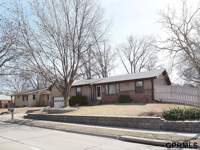 ranch-style home featuring board and batten siding, a garage, fence, and brick siding