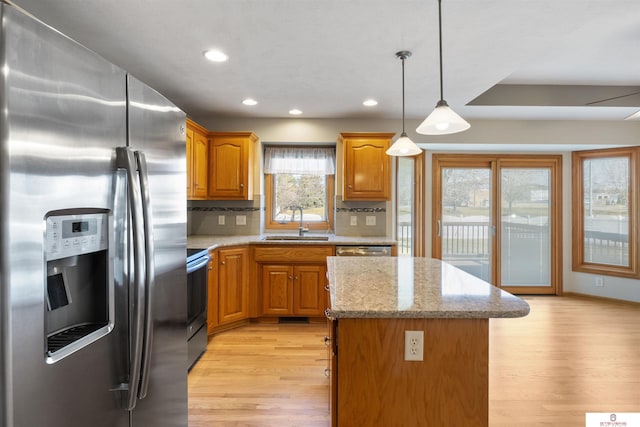 kitchen with light stone counters, light wood-type flooring, a sink, stainless steel appliances, and brown cabinets