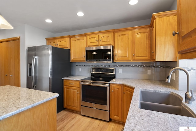 kitchen with light wood finished floors, backsplash, recessed lighting, appliances with stainless steel finishes, and a sink