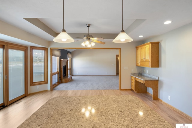 kitchen featuring baseboards, a tray ceiling, recessed lighting, hanging light fixtures, and light wood-type flooring