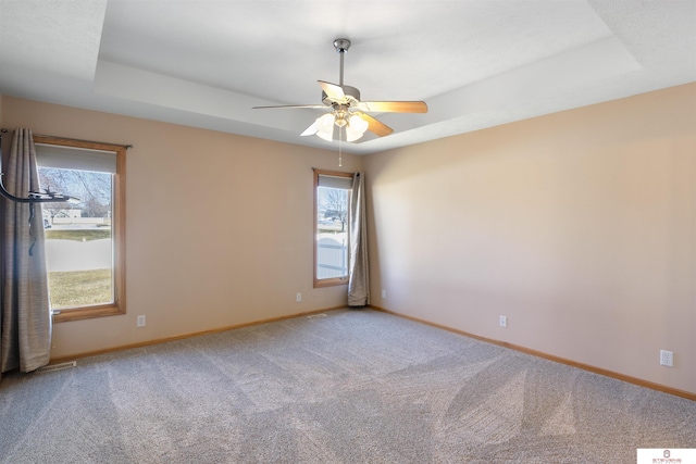 carpeted empty room with a tray ceiling, baseboards, and ceiling fan