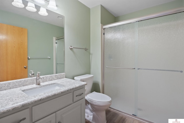 bathroom featuring a stall shower, toilet, vanity, and wood finished floors