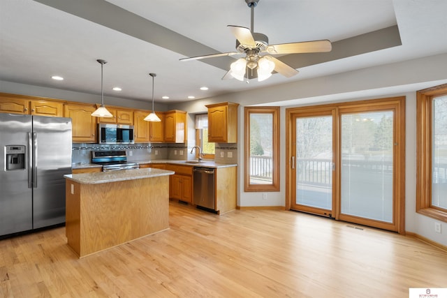 kitchen featuring light wood-type flooring, a sink, tasteful backsplash, a kitchen island, and appliances with stainless steel finishes