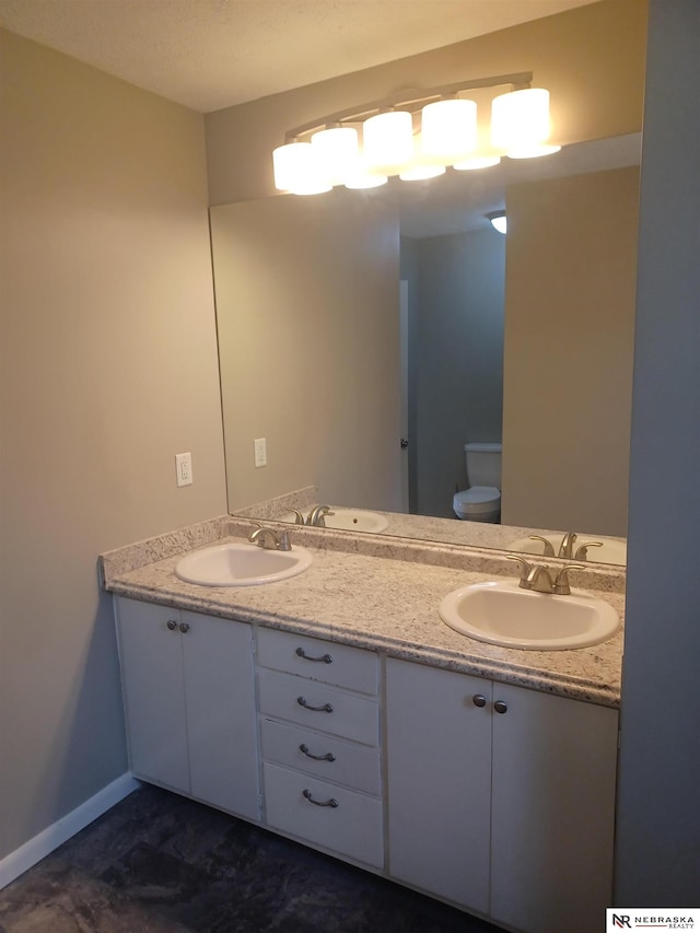 bathroom featuring double vanity, toilet, baseboards, and a sink