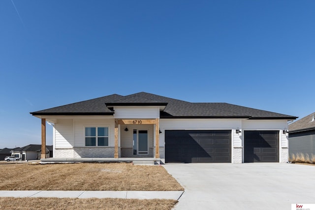 prairie-style house with brick siding, concrete driveway, an attached garage, and a shingled roof