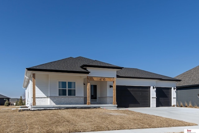 view of front facade with a front yard, an attached garage, a shingled roof, concrete driveway, and brick siding