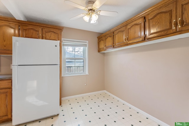 kitchen with brown cabinetry, light floors, freestanding refrigerator, and baseboards